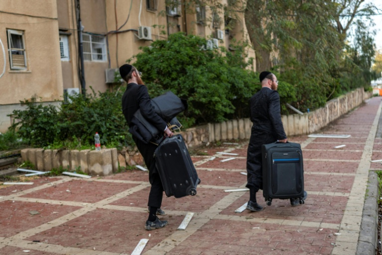 Des juifs orthodoxes transportent des effets personnels de leur domicile endommagé après un tir de missile iranien, le 22 mars 2026 à Arad, dans le sud d'Israël  ( AFP / Ilia YEFIMOVICH )
