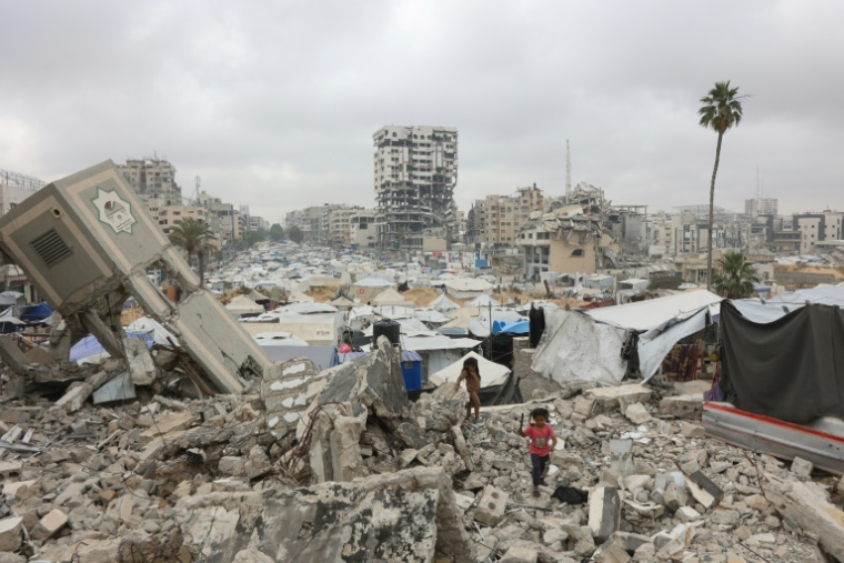 Des fillettes palestiniennes marchent dans un camp de déplacés de fortune installé au milieu des décombres de bâtiments dans la ville de Gaza, le 12 mai 2025 ( AFP / Omar AL-QATTAA )