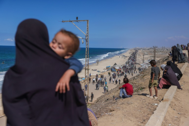 Une Palestinienne portant un enfant regarde les gens marcher le long d'une route côtière, dans le centre de la bande de Gaza, en diection du nord, le 10 octobre 2025 ( AFP / BASHAR TALEB )