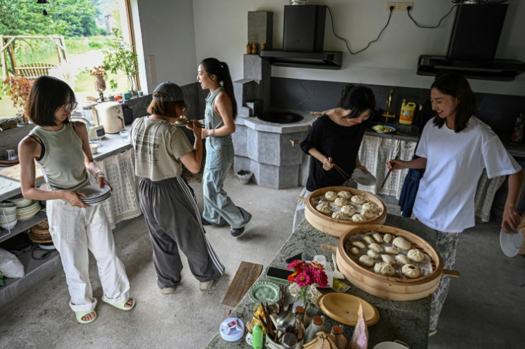Chen Yani (d), fondatrice du lieu "L'Univers imaginaire de Keke", déjeune avec des participantes dans la cuisine du gîte rural, le 14 juillet 2025 à Hangzhou, dans la province du Zhejiang, dans l'est de la Chine ( AFP / Jade GAO )