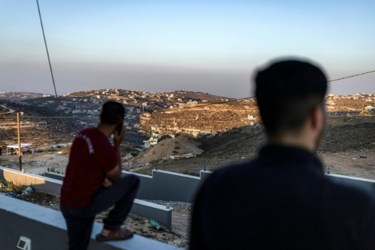 Des hommes palestiniens observent des soldats de l'armée israélienne depuis le toit d'une des maisons assiégées par des colons israéliens dans le village de Qusra, en Cisjordanie, le 18 août 2026 ( AFP / ilia YEFIMOVICH )