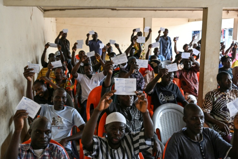 Des producteurs de cacao brandissent des reçus montrant qu'ils n'ont toujours pas été payés, lors d'une réunion avec les coopératives d'achat, à Songan, un village près d'Aboisso, dans le sud ivoirien, le 17 mars 2026 ( AFP / Sia KAMBOU )