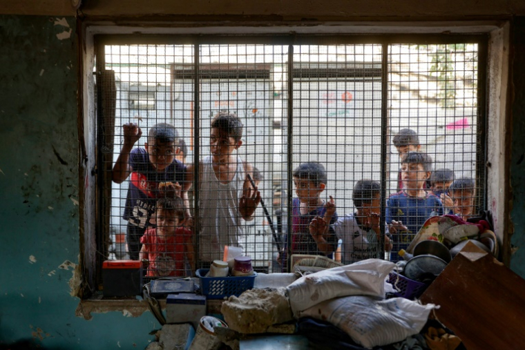 Des enfants palestiniens regardent depuis le grillage d'une salle de classe endommagée de l'école al-Farabi transformée en abri pour déplacés, après avoir été touchée par une frappe israélienne dans la ville de Gaza, le 7 septembre 2025 ( AFP / Omar AL-QATTAA )
