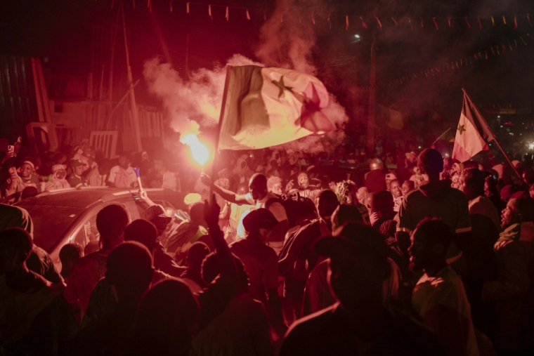 Des supporters sénégalais brandissent le 18 janvier 2026 à Dakar un drapeau du pays en célébrant la victoire de l'équipe de football sénégalaise face au Maroc en finale de  CAN-2025, le 18 janvier 2026 à Dakar  ( AFP / Carmen Abd Ali )