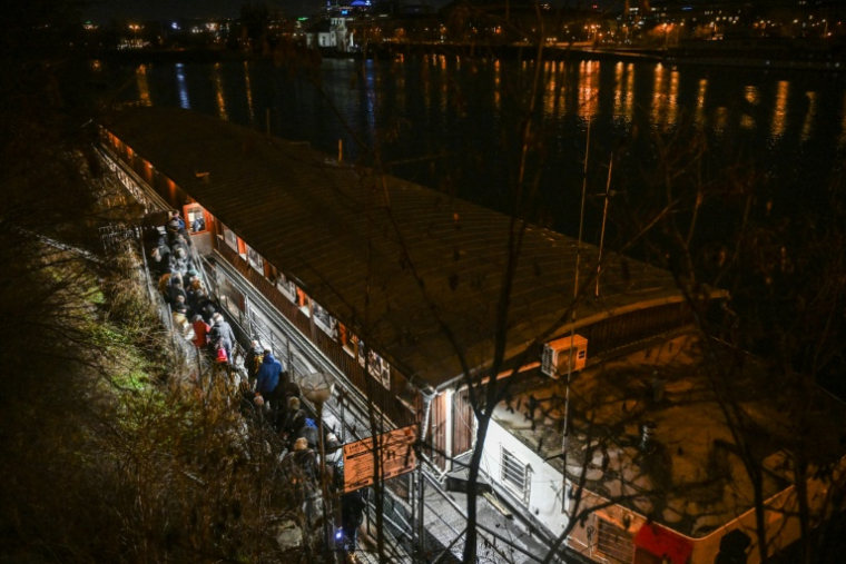 Des personnes font la queue pour passer la nuit sur l'Hermes, une péniche amarrée près de l'un des nombreux ponts qui enjambent la rivière Vltava à Prague, où le nombre de sans-abri connaît une augmentation inquiétante, le 26 janvier 2026 ( AFP / Michal Cizek )