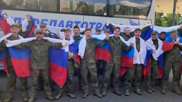 Image tirée d'une vidéo distribuée par le ministère russe de la Défense, le 10 juin 2025, de prisonniers de guerre russes enveloppés dans des drapeaux nationaux devant un bus après un échange dans un lieu non divulgué au Bélarus ( Ministère russe de la Défense / Handout )