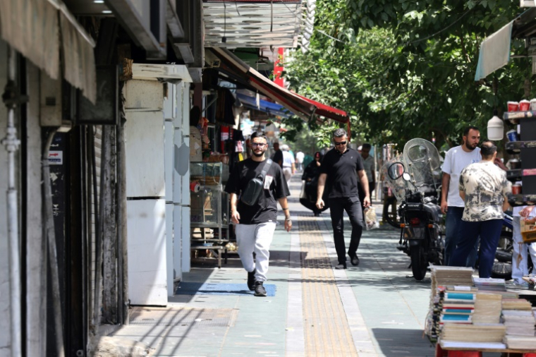 Des Iraniens passent devant une boutique sur la place Enghelab (Révolution), à Téhéran, le 24 juin 2025 ( AFP / ATTA KENARE )