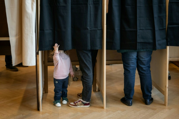 Un enfant dans l'isoloir où son père vote pour le premier tour des municipales, le 15 mars 2026 à Lyon ( AFP / ARNAUD FINISTRE )