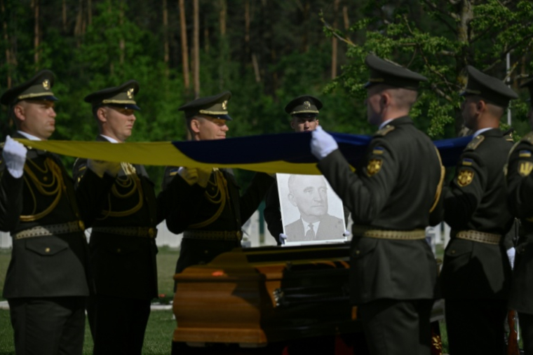 Des militaires de la garde d’honneur ukrainienne tiennent des drapeaux nationaux au-dessus des cercueils contenant les dépouilles d’Andriy Melnyk, mort en 1964 et chef d’une branche de l’Organisation des nationalistes ukrainiens (OUN) lors de leur cérémonie de réinhumation au cimetière militaire national près de Kiev, le 25 mai 2026 ( AFP / Genya SAVILOV )