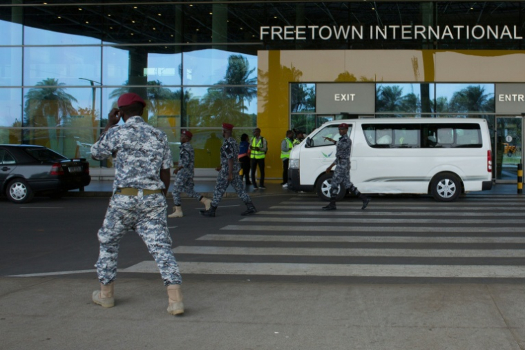 Des agents de sécurité escortent des migrants vers un centre de l'Agence nationale de santé publique (NPHA) après leur arrivée à l'aéroport international de Freetown, le 20 mai 2026 à Lungi, en Sierra Leone ( AFP / - )