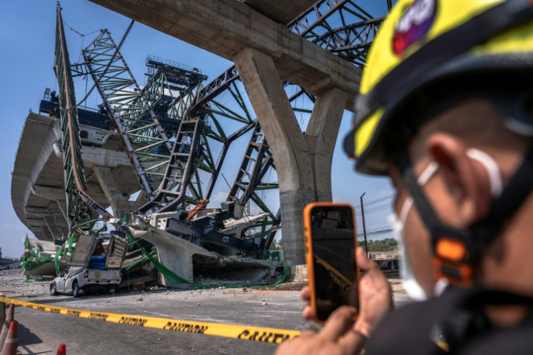 Un secouriste prend des photos là où une grue de chantier s'est effondrée sur une autoroute à Samut Sakhon, dans la banlieue de Bangkok, le 15 janvier 2026 ( AFP / Chanakarn Laosarakham )