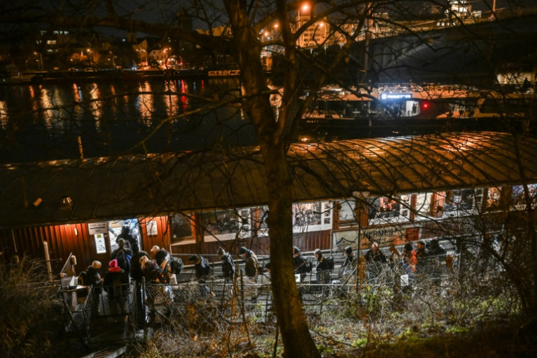 Des personnes font la queue pour passer la nuit sur l'Hermes, une péniche amarrée près de l'un des nombreux ponts qui enjambent la rivière Vltava à Prague, où le nombre de sans-abri connaît une augmentation inquiétante, le 26 janvier 2026 ( AFP / Michal Cizek )