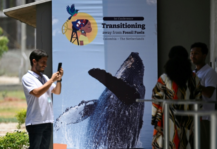 Des personnes prennent une photo devant une affiche de la conférence pour une sortie des énergies fossiles, à Santa Marta, en Colombie, le 26 avril 2026 ( AFP / Raul ARBOLEDA )