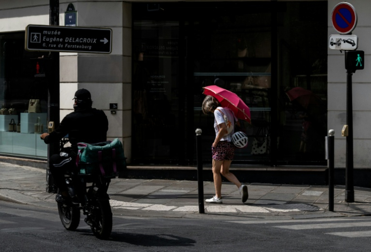 Une passante se protège du soleil avec un parapluie dans une rue à Paris, le 13 juillet 2026 lors d'un épisode de canicule en France ( AFP / Martin LELIEVRE )