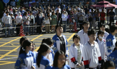 Des lycéens attendent d'entrer dans la salle d'examen pour passer le "gaokao", le concours national d'entrée à l'université, sous les regards de leurs parents maintenus derrière un cordon à l'arrière-plan, le 7 juin 2026 à Pékin ( AFP / WANG Zhao )