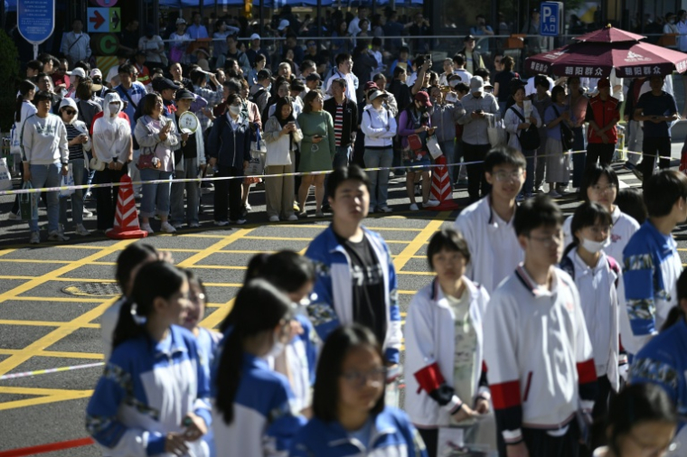 Des lycéens attendent d'entrer dans la salle d'examen pour passer le "gaokao", le concours national d'entrée à l'université, sous les regards de leurs parents maintenus derrière un cordon à l'arrière-plan, le 7 juin 2026 à Pékin ( AFP / WANG Zhao )