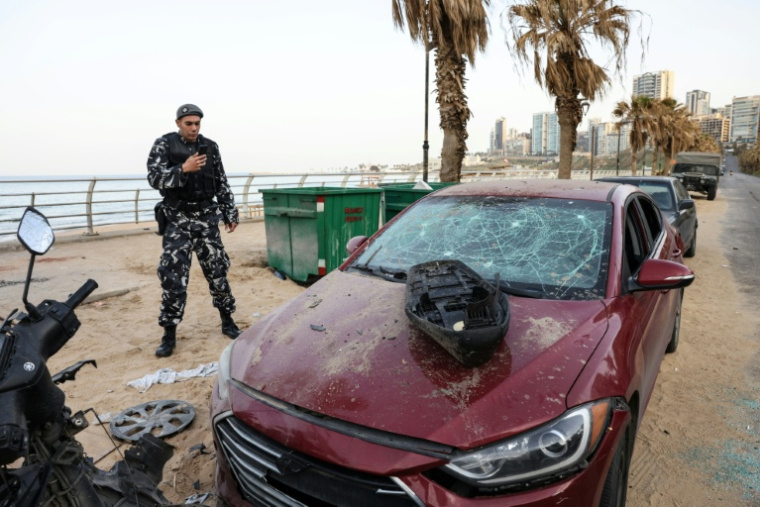 Un policier observe une voiture endommagée sur le site d'une frappe aérienne israélienne dans la zone côtière de Ramlet al-Bayda à Beyrouth, le 12 mars 2026 au Liban ( AFP / Anwar AMRO )