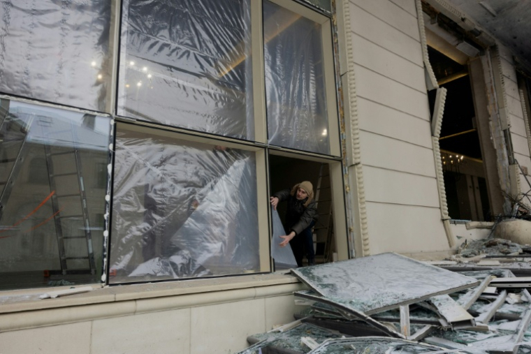 Un homme couvre avec du plastique des fenêtres brisées après une attaque russe, le 9 janvier 2026 à Kiev ( AFP / Tetiana DZHAFAROVA )