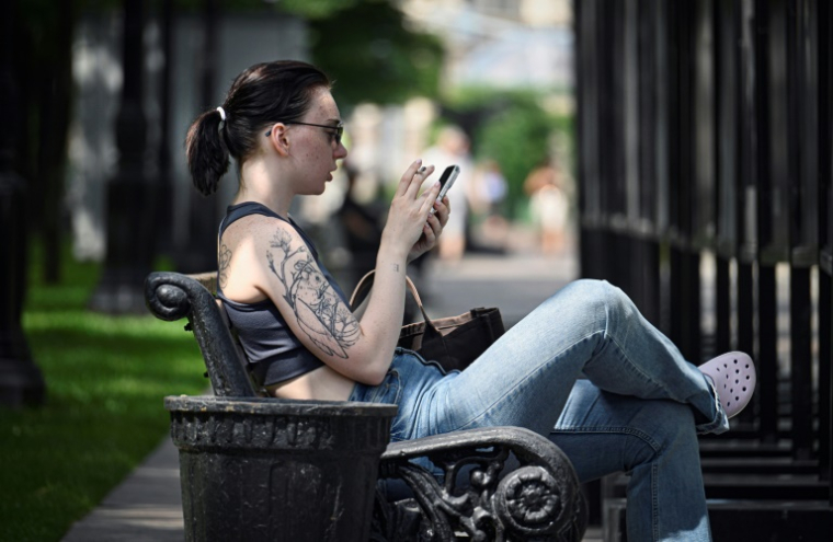 Une femme assise sur un banc utilise son smartphone à Moscou, le 30 juillet 2025 ( AFP / Alexander NEMENOV )