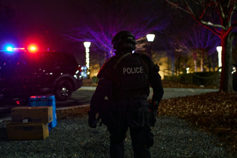 Un policier devant un bus transportant des étudiants évacués vers un site temporaire après des tirs à l'université Brown à Providence, le 13 décembre 2025 dans l'Etat de Rhode Island ( AFP / Bing Guan )