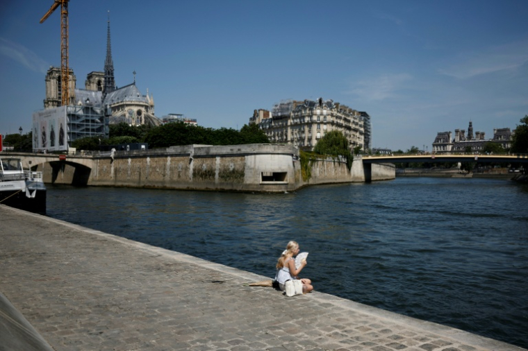 Une femme, assise sur les quais de la Seine, se rafraîchit avec un éventail lors d'une vague de chaleur précoce, le 28 mai 2026 à Paris ( AFP / SIMON WOHLFAHRT )