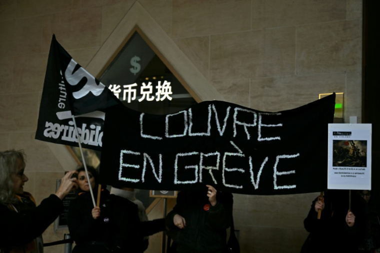 Des salariés du Louvre brandissent une bannière devant l'entrée du musée, à Paris le 15 décembre 2025 ( AFP / Blanca CRUZ )