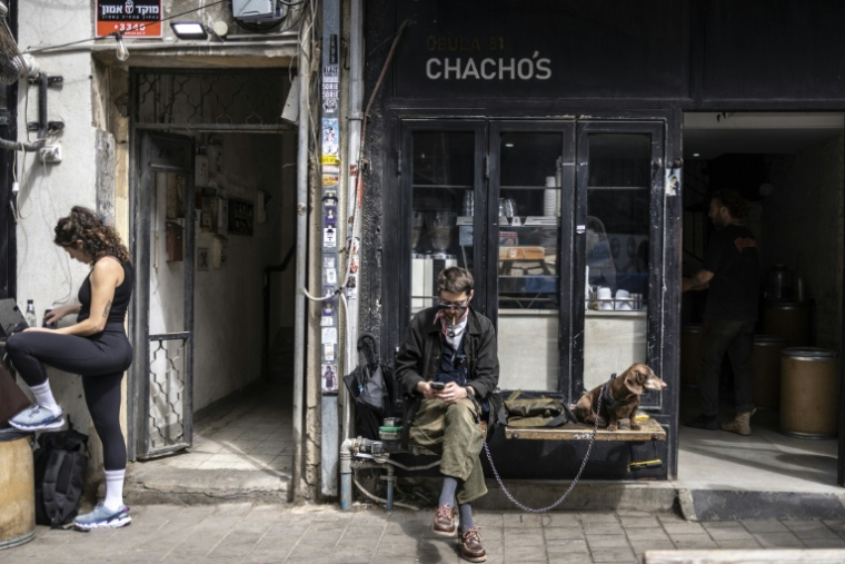 Un client est assis devant un café avec son chien dans la ville côtière israélienne de Tel Aviv, le 9 mars 2026.  ( AFP / OLYMPIA DE MAISMONT )