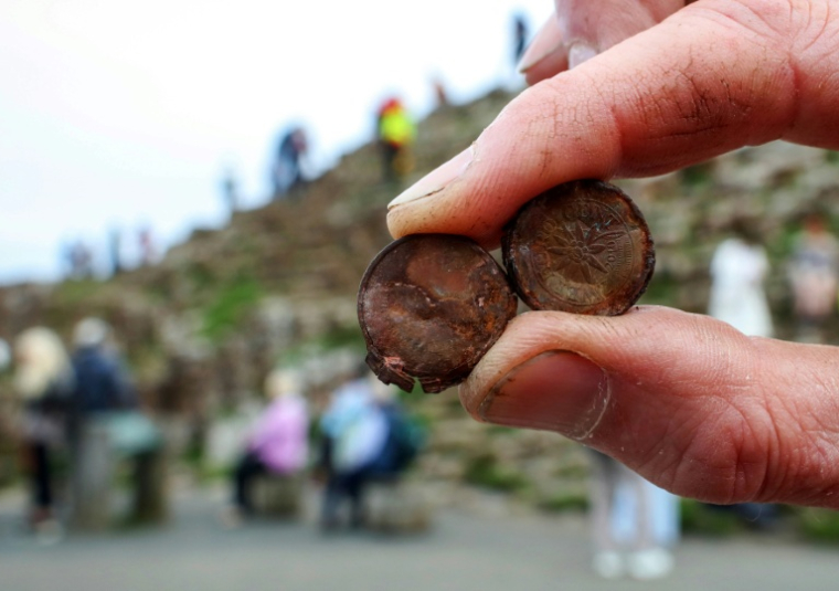 Cliff Henry, du National Trust, montre des pièces de monnaie rouillées laissées par les touristes sur le site de la Chaussée des Géants près de Bushmills en Irlande du Nord, le 8 juillet 2025 ( AFP / PAUL FAITH )