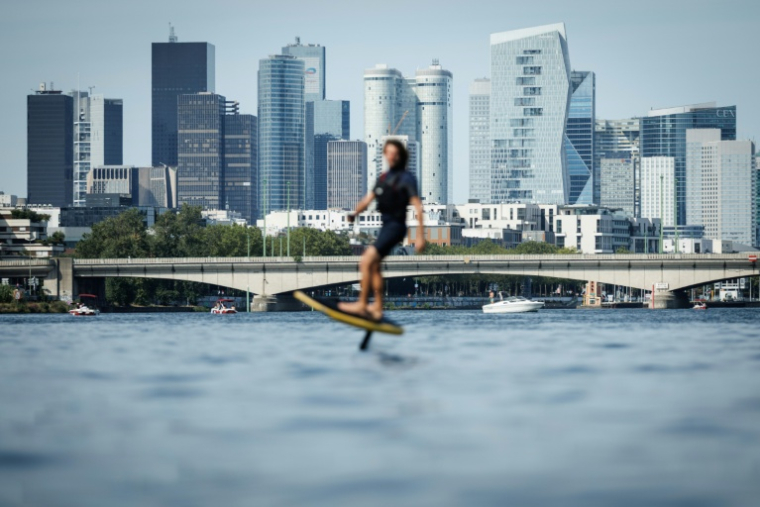 Le moniteur d'e-foil et cofondateur du club Foil in Paris Nicolas Pernodet sur son surf électrique sur la Seine, devant le quartier d'affaires de La Défense, à Paris, le 2 août 2026 ( AFP / Simon WOHLFAHRT )
