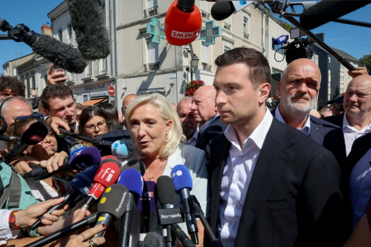 Marine Le Pen (c), cheffe du groupe parlementaire Rassemblement national (RN) et candidate à la présidentielle de 2027, et Jordan Bardella, président du RN, entourés de journalistes à leur arrivée à La Flèche pour un rassemblement de campagne, le 8 juillet 2026 dans la Sarthe ( AFP / FRED TANNEAU )