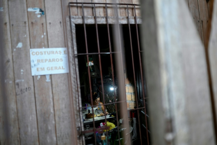 Une femme travaille devant sa machine à coudre chez elle à Vila da Barca, un quartier pauvre bâti sur pilotis sur les rives du fleuve Guama à Belem, dans l'État du Para, le 5 novembre 2025 au Brésil ( AFP / Mauro PIMENTEL )