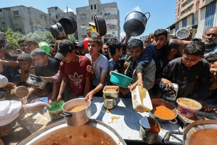 Des Palestiniens font la queue pour obtenir un repas chaud lors d'une distribution assurée par une cuisine soldiaire au camp de réfugiés de Nousseriat, dans le centre de la bande de Gaza, le 5 mai 2025 ( AFP / Eyad BABA )