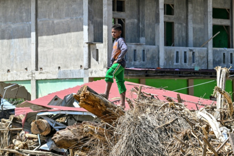 Un enfant debout sur des débris d'arbres après des crues soudaines à Meureudu, dans province d'Aceh, en Indonésie, le 8 décembre 2025 ( AFP / CHAIDEER MAHYUDDIN )