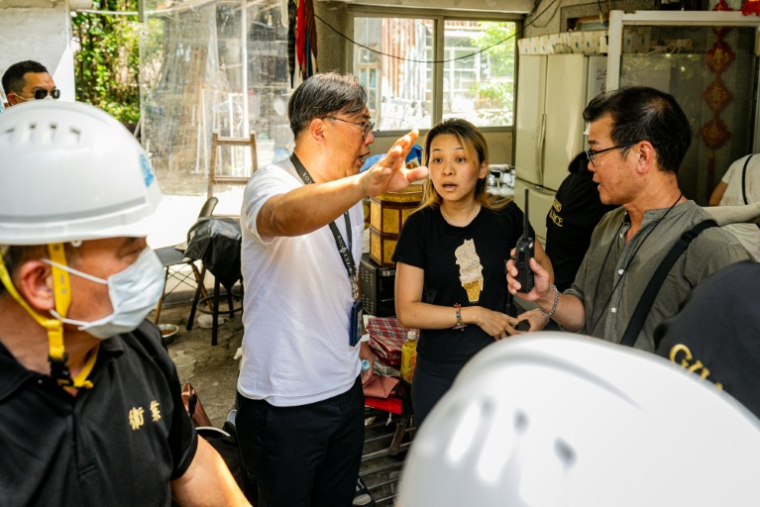 Un policier en civil demande à Niki So, une habitante d'un village de Kwu Tung, de quitter son domicile qui doit être démoli pour faire place à un vaste projet de pôle technologique, le 23 juin 2026 dans les Nouveaux Territoires à Hong Kong ( AFP / Leung Man Hei )