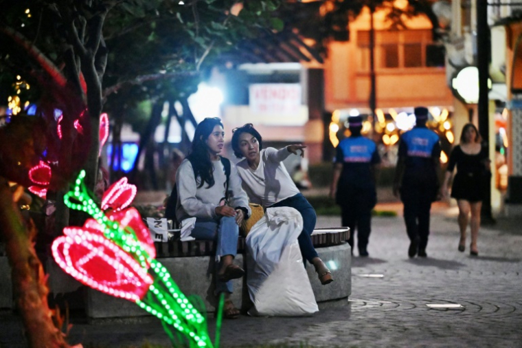 Deux femmes assises sur un banc pendant que des agents de sécurité municipaux patrouillent dans une rue de Guayaquil, en Équateur, le 9 août 2025 ( AFP / MARCOS PIN )