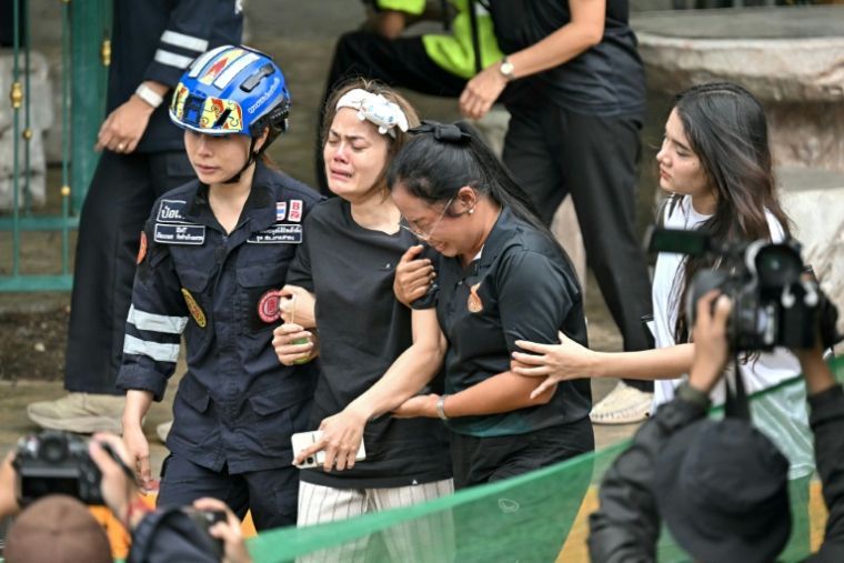 L'épouse (C) d'un professeur tué par un adolescent dans un lycée au nord de Bangkok est emmenée vers une ambulance, dans le district de Bang Kruai, en Thaïlande, le 7 août 2026 ( AFP / Lillian SUWANRUMPHA )