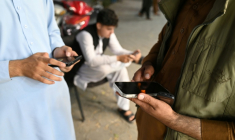 Des Afghans consultent leurs téléphones portables, le 1er octobre 2025 à Kaboul ( AFP / Wakil KOHSAR )