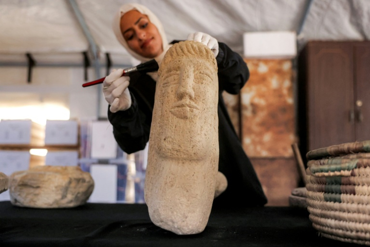 Une membre de l'association Mayasem pour la culture et les arts nettoie un artefact à la brosse, sous une tente à Khan Younès, dans le sud de la bande de Gaza, le 11 juillet 2026 ( AFP / Bashar Taleb )