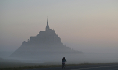 Un cycliste passe devant le Mont-Saint-Michel, enveloppé par la brume matinale, le 9 juillet 2025 ( AFP / Damien MEYER )