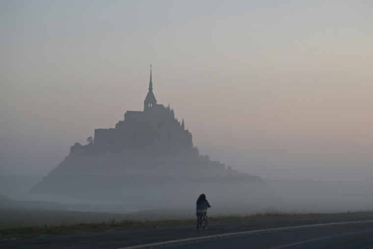 Un cycliste passe devant le Mont-Saint-Michel, enveloppé par la brume matinale, le 9 juillet 2025 ( AFP / Damien MEYER )
