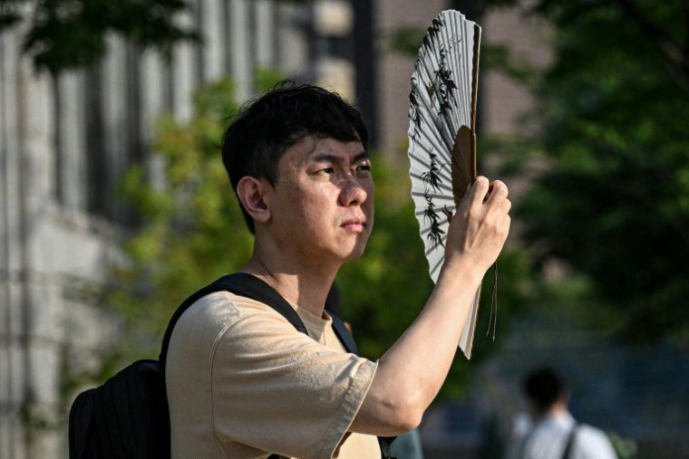 Un homme se protège du soleil avec un éventail, le 13 juillet 2026 à Séoul  ( AFP / JADE GAO )