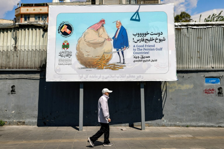 Un homme marche sous une banderole représentant un dessin satirique montrant le président américain Donald Trump serrer la main d'un dirigeant non identifié d'un pays du Golfe dans une rue de Téhéran le 6 avril 2026 ( AFP / ATTA KENARE )