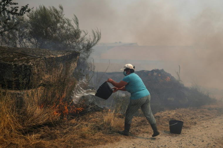 Une femme tente d'éteindre des flammes à l'aide d'un seau d'eau le 15 août 2025, dans le village d'Antas, au Portugal ( AFP / PATRICIA DE MELO MOREIRA )