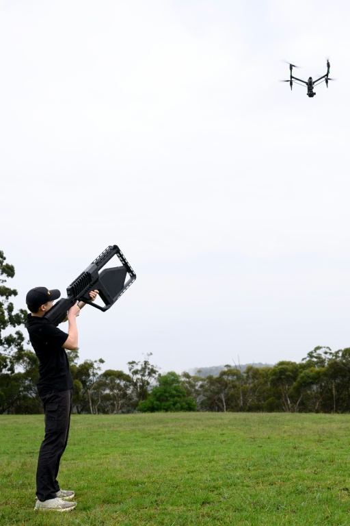 Un membre de l'équipe DroneShield pointe le fusil "DroneGun" vers un drone à Sydney, le 9 février 2026 en Australie ( AFP / STEVEN MARKHAM )