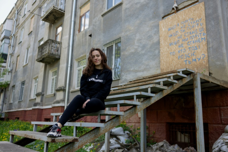 La reporter de guerre ukrainienne, Alina Yevych, assise sur les marches d'un bâtiment endommagé à Kramatorsk, dans la région de Donetsk, le 11 mai 2025 ( AFP / Tetiana DZHAFAROVA )