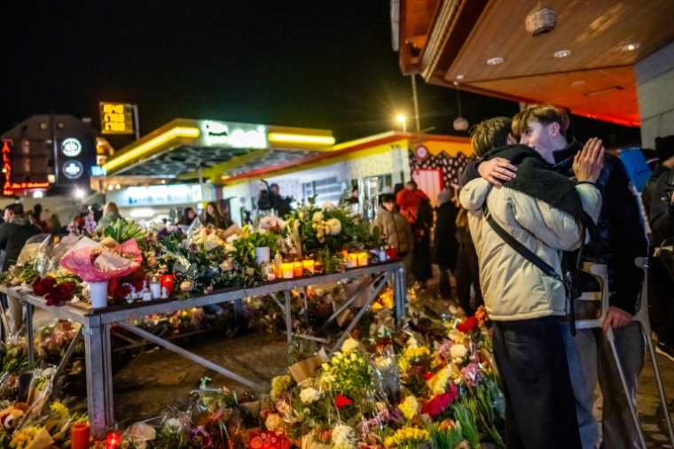 Un survivant blessé (à droite) enlace un proche près d'un mémorial improvisé après un incendie dans un bar qui a fait 40 morts et plus de 100 blessés au nouvel an, à Crans-Montana (Suisse) le 2 janvier 2026 ( AFP / MAXIME SCHMID )
