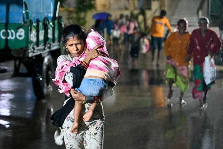Une personne avec un enfant arrive vers un abri à l'approche du cyclone Arnab, à Kakinada en Inde, le 27 octobre 2026 ( AFP / Noah SEELAM )