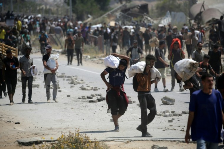 Des Palestiniens transportent des sacs d'aide humanitaire, dans le camp de Nousseirat, dans le centre de la bande de Gaza, le 27 juillet 2025 ( AFP / Eyad BABA )
