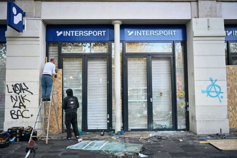 Des employés installent des panneaux en bois sur la vitrine brisée d'un magasin au landemain d'une manifestation contre la vie chère, le 18 octobre 2026 à Paris ( AFP / Matthieu RONDEL )