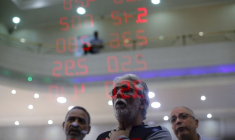 Des hommes réagissent en lisant un tableau affichant les taux de change du real brésilien par rapport au dollar américain et à plusieurs devises étrangères à Rio de Janeiro